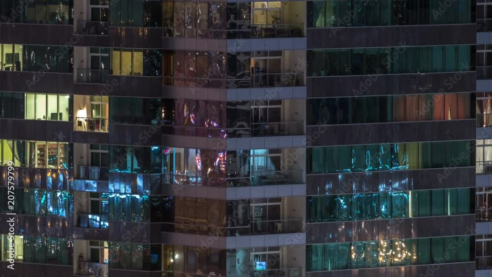 Windows of the multi-storey building of glass and steel lighting inside and moving people within timelapse