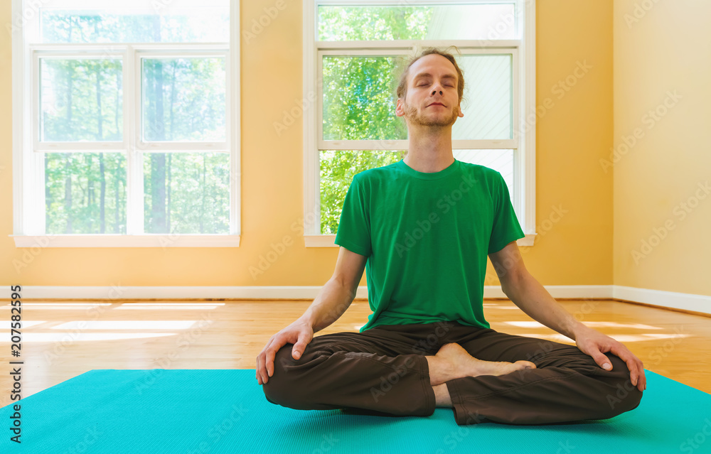 Man in a meditation pose inside a big bright room Man in a meditation pose inside a big bright room