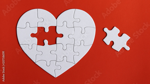 A missing piece of the puzzle and puzzles in the shape of a white heart on the red background.