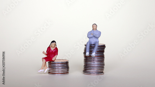 Concept of difference in pay between men and women. A miniature man and a woman sitting on a pile of coins.