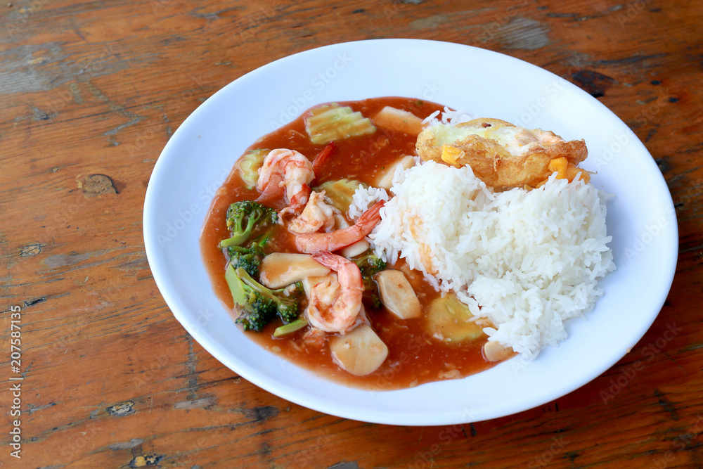 stir fried shrimp and Broccoli in thai red curry paste sauce with rice, Curry fried shrimps and cooked rice in white dish closeup on wooden table. Thai style food.