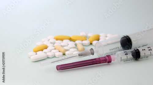 Close-up image of two disposable medical syringes and pills.