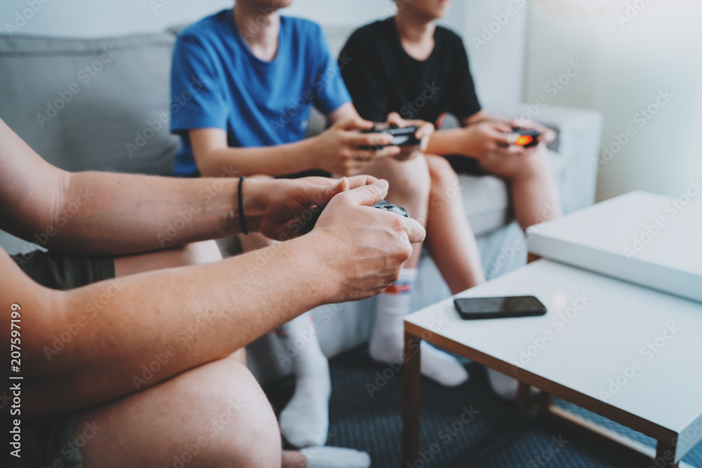 Young teenage sitting on a sofa in living room and playing video games. Family relaxing time at home concept. Closeup. Young teenage sitting on a sofa in living room and playing video games. Family relaxing time at home concept. Closeup.