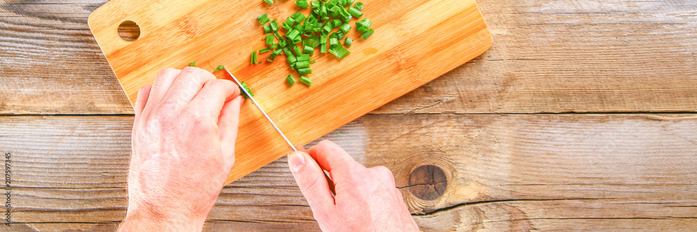 Male hands cut a green onion on a cutting board on an old wooden table. Male hands cut a green onion on a cutting board on an old wooden table.