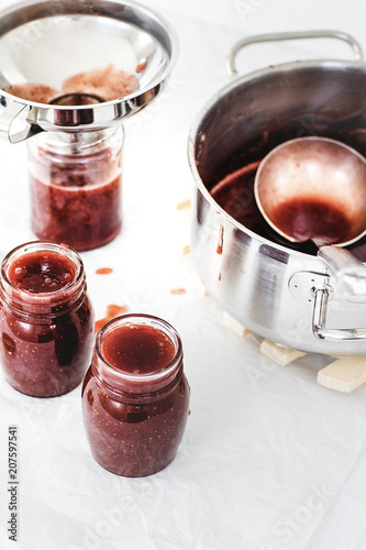 Preparing marmalade at home. Fresh red fruits from own garden or farmer market. Self supply, traditional canning with boiling in sugar. Filling glass jars with hot jam.