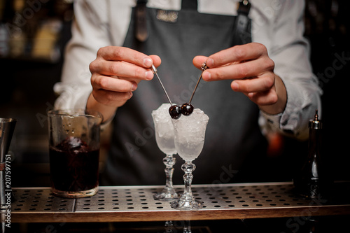 фотографія Bartman hands decorating two cocktail glasses with cherries