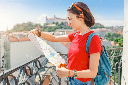 A young happy girl traveler looks at the map and tries to find the right direction for the next attraction in the European city