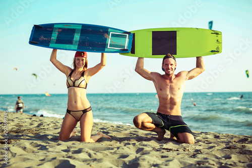 Pretty smiling Caucasian woman kitesurfer enjoying summertime on sandy beach with her boyfriend.