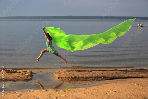 Młoda dziewczynka skacze przez wodę z długą zieloną chustą.