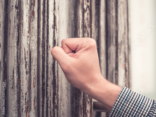 sunburned hand of a man in a plaid shirt pounding his fist in the old and shabby front door.