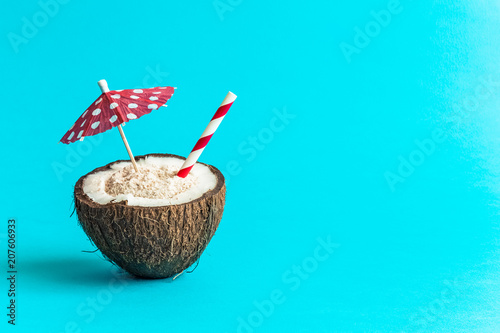 Coconut with paper parasol and drinking straw isolated on blue background. Space for copy.