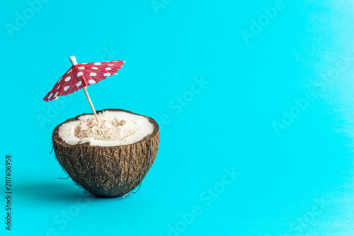 Coconut with paper parasol isolated on blue background. Space for copy.