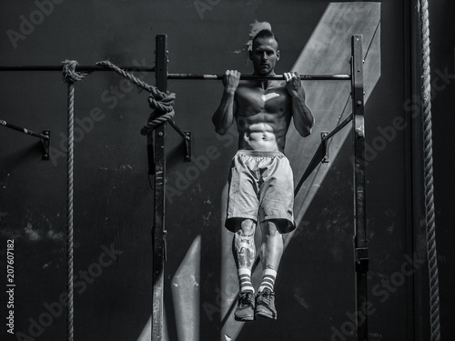 Blond, attractive young man hanging from gym equipment, looking at camera