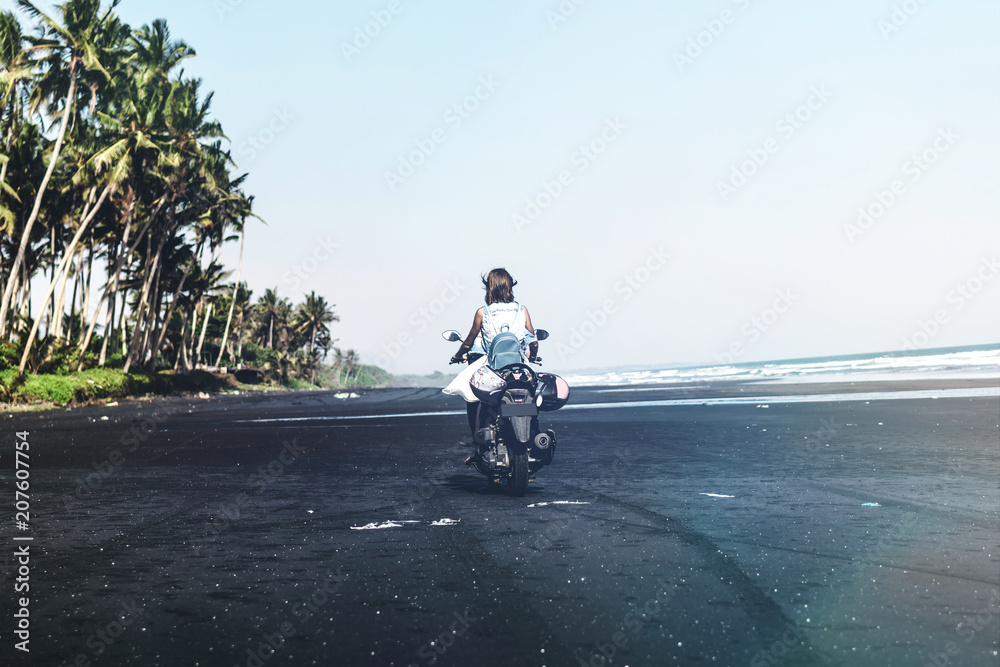 Obraz premium Young woman driving a scooter at the beach with black sand. Bali island.