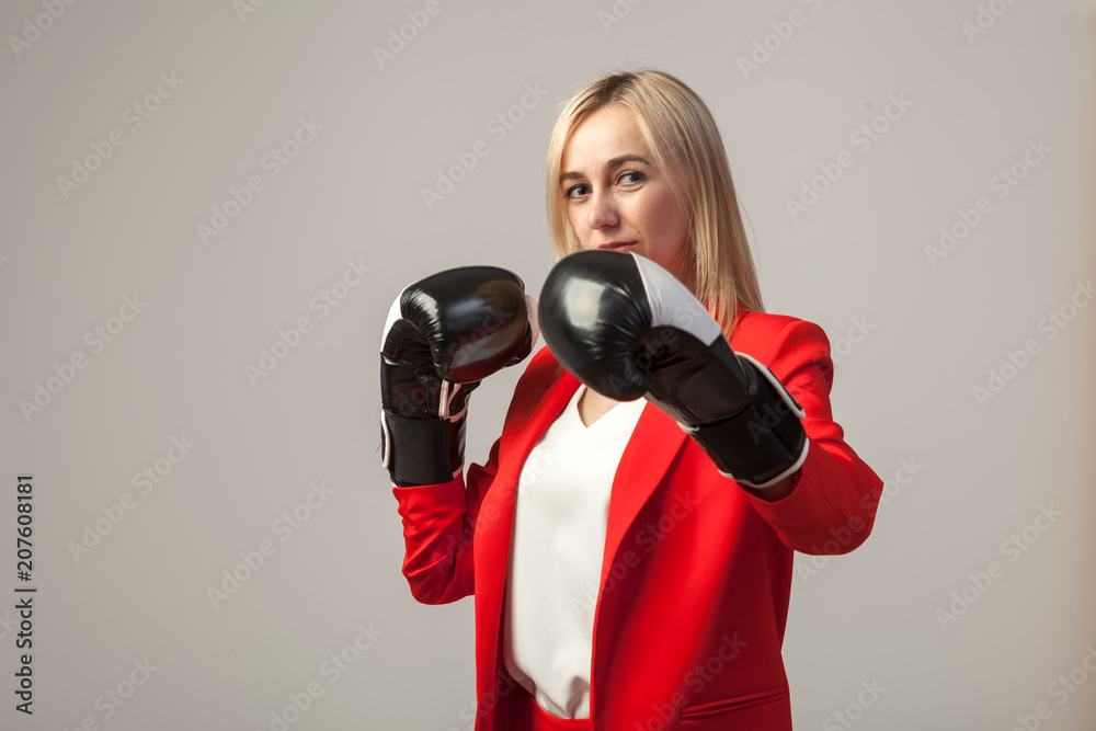 Young beautiful white blond girl in a bright red strict suit with a jacket and white blouse standing in a pose with boxing gloves on a white isolated background Young beautiful white blond girl in a bright red strict suit with a jacket and white blouse standing in a pose with boxing gloves on a white isolated background