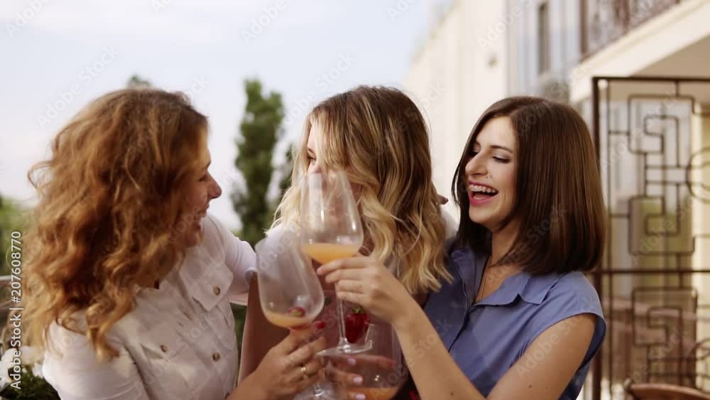 Concept of hen-party. Three beautiful women drinking cocktails together on a terrace. Women chatting and laughing. Slow motion Concept of hen-party. Three beautiful women drinking cocktails together on a terrace. Women chatting and laughing. Slow motion