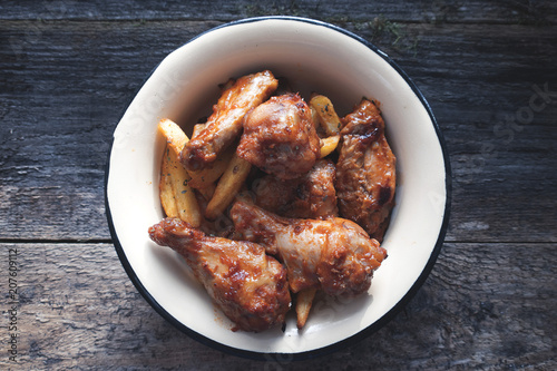 Appetizing chicken pieces and french fries with seasoning in a beautiful old bowl and on an old wooden background