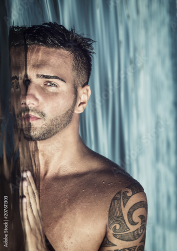 Attractive young shirtless athletic man standing in water in sea or lake, with half face submerged underwater, looking at camera
