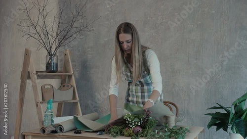 Beautiful long blonde hair female florist preparing wrapping paper for packaging flower bouquet arrangement in flower shop. Florist making floral arrangement at her workplace. photo