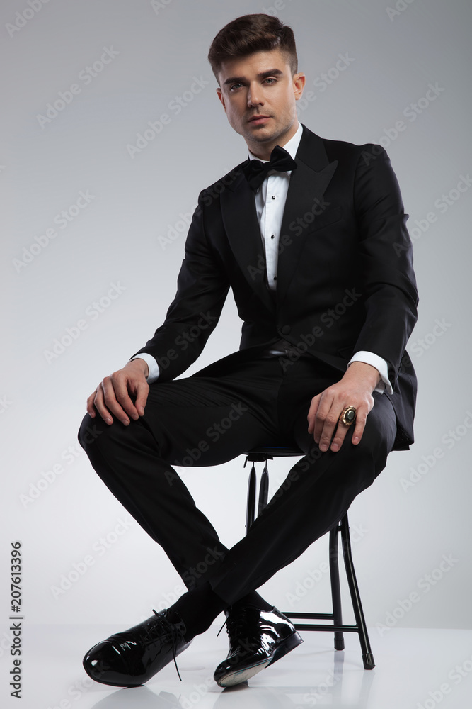handsome man in tuxedo resting on metal chair