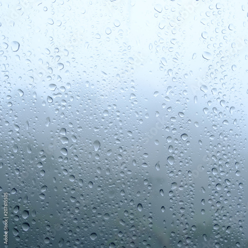 Rain drops on window glasses surface with cloudy and green background .