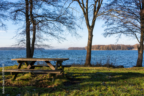wooden bench on the green grass, lake and blue sky background