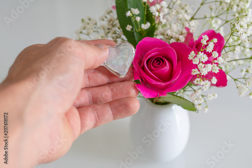 Herz in der Hand vor Rosenstrauss in Vase auf weiß