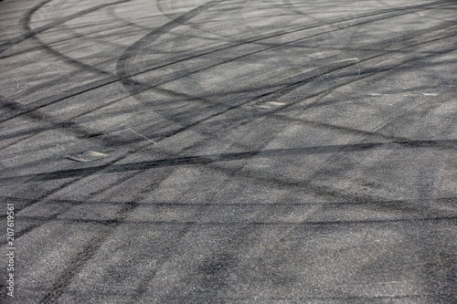 Abstract transportation background with turning black tire tracks over dark asphalt road pavement