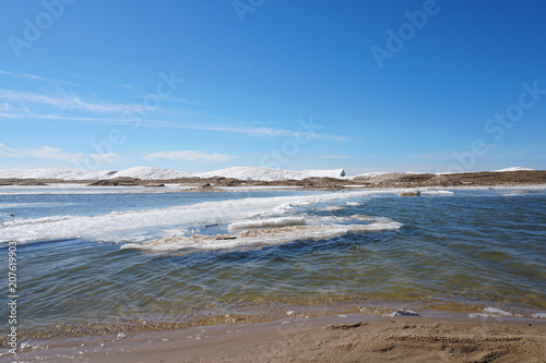 Beaurtiful sunny day along the lake shore on spring day with ice and snow in water, blue sky in the background, sandy beach in foreground