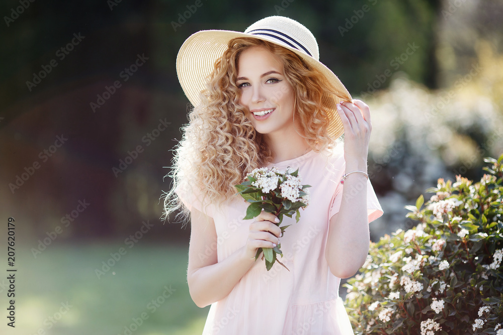 Beautiful young model spring girl in flowers with hairstyle in summer  blossom park. Woman in a blooming garden. Portrait of a beautiful woman  with curly hair outdoors in a spring park Stock