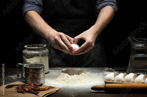 Hands are cracking an egg into flour to make dough on wooden table