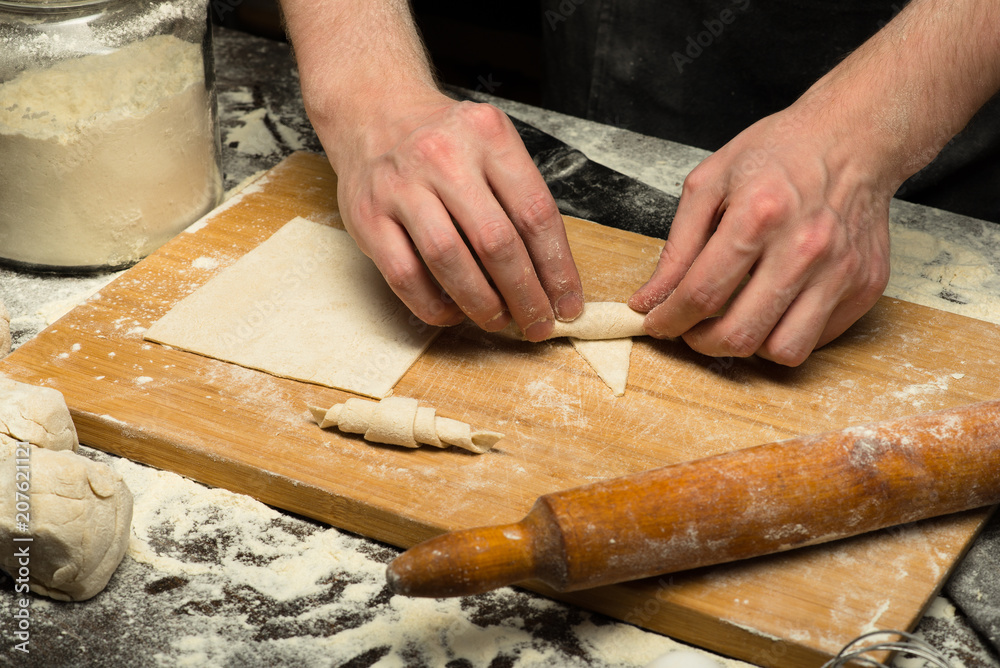 Chef hands are rolling a croissant from dough on wooden board. black background. close-up view Chef hands are rolling a croissant from dough on wooden board. black background. close-up view