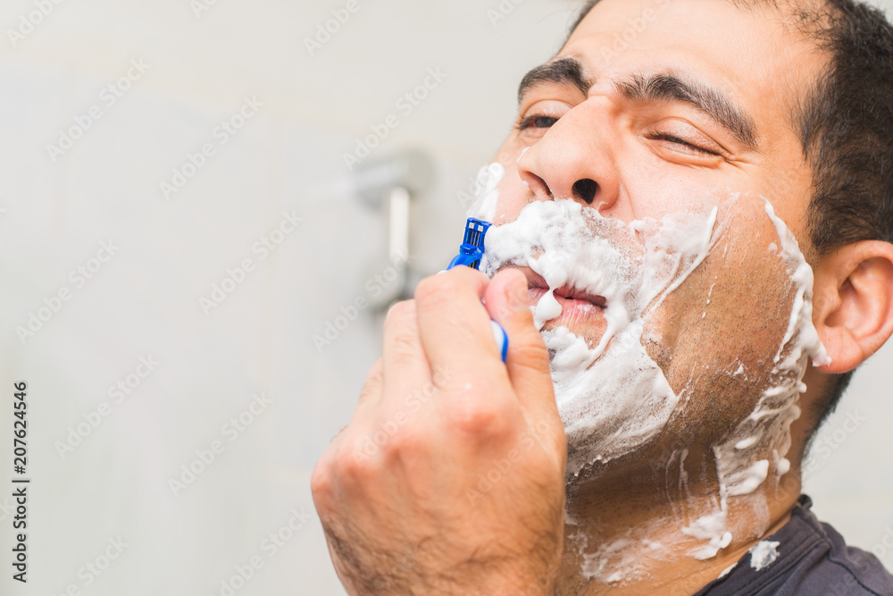 man shaves his beard with a razor