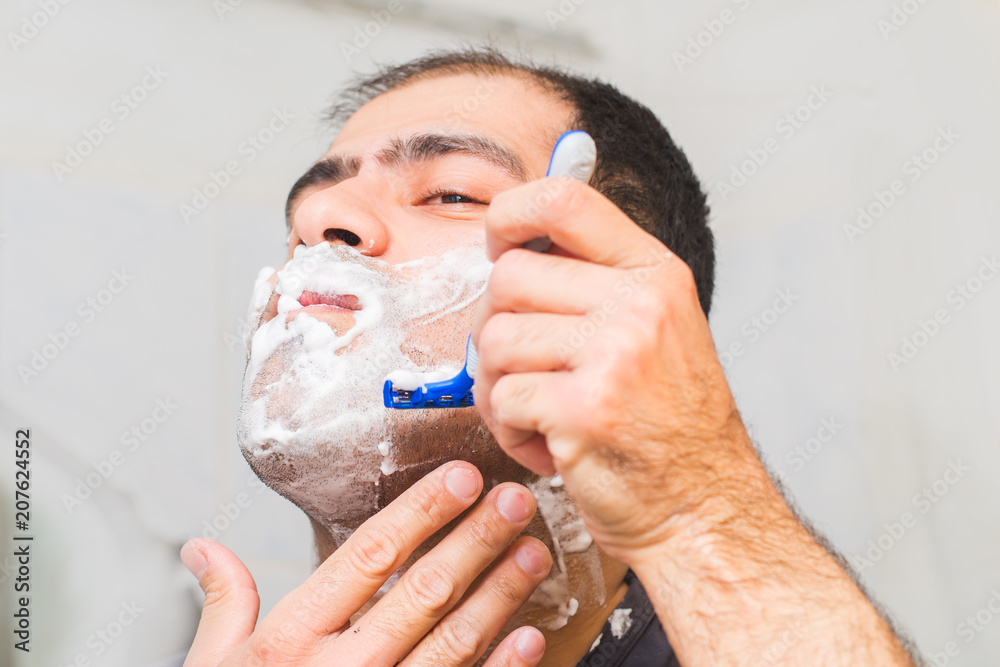 man shaves his beard with a razor