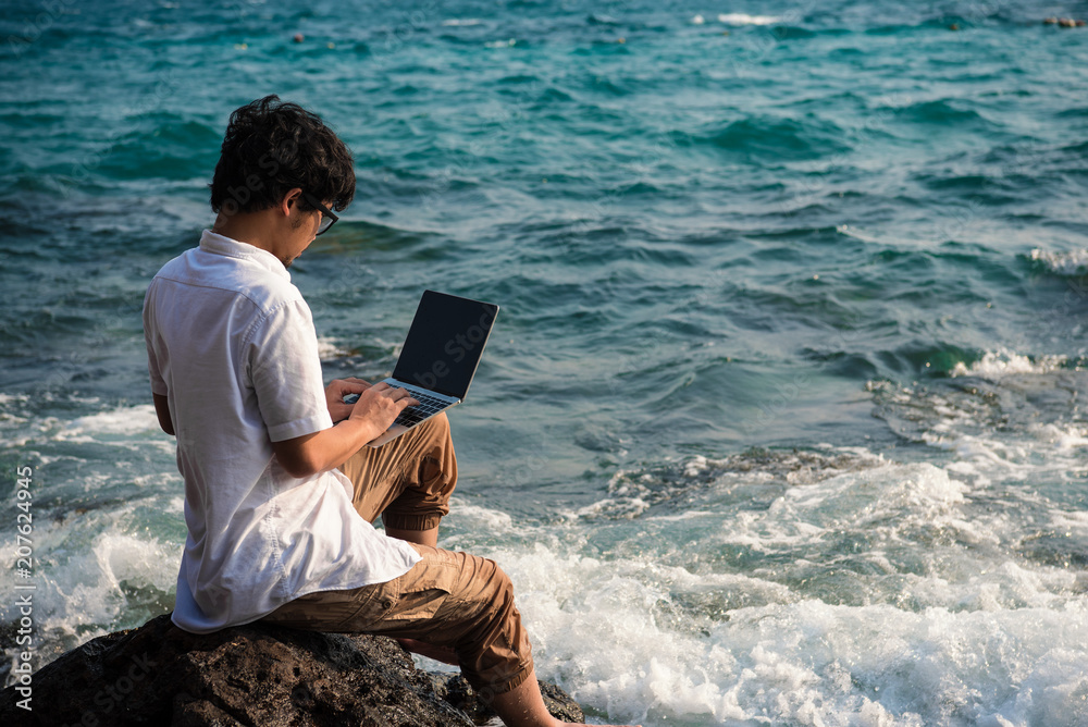 man with computer laptop is  ecstatic with success and feeling confidence on rocks on the sea