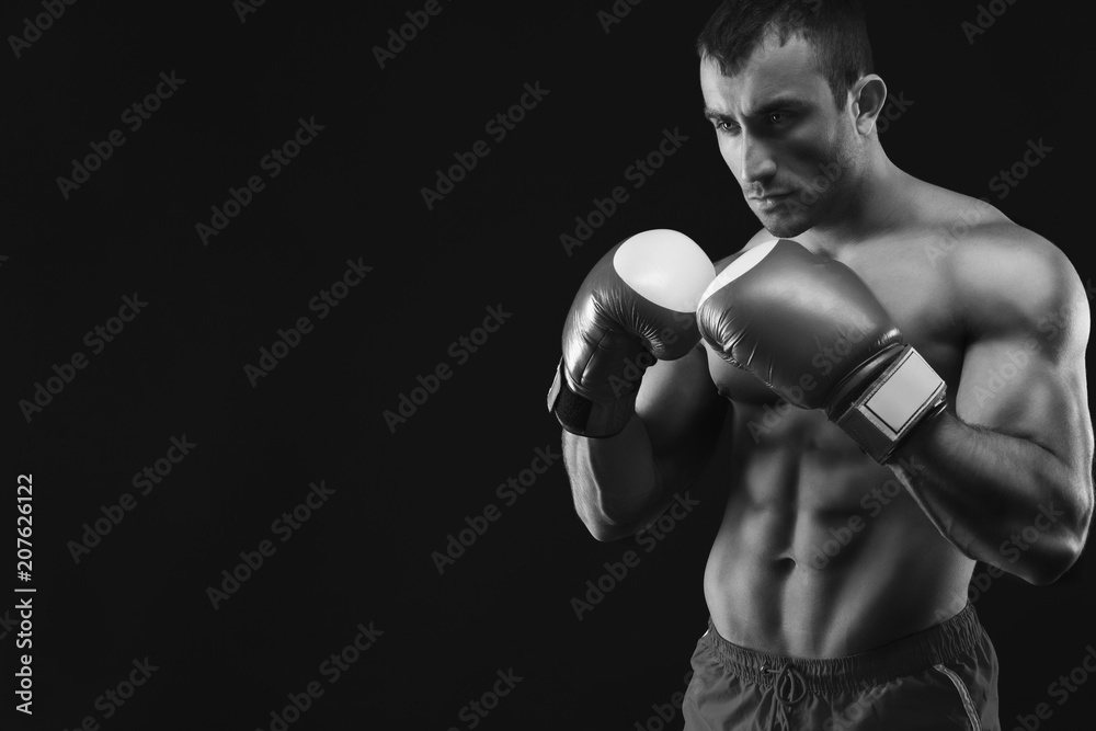 Muscular man in boxing gloves at black background
