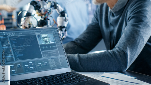 Robotics Engineer Manipulates Voice Controlled Robot, Laptop Screen Shows Speech and Face Recognition Software. In the Background Robotics Reseatch Center Laboratory. photo