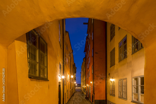 Night view of narrow alley connecting with archway passage street with historic town houses of colored facade illuminated by lights in the Old city (Gamla Stan) of Stockholm, Sweden.