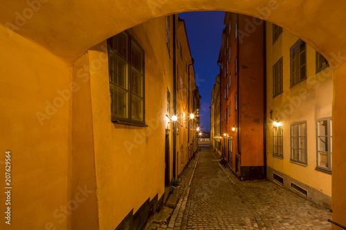 Night view of narrow alley connecting with archway passage street with historic town houses of colored facade illuminated by lights in the Old city  Gamla Stan  of Stockholm  Sweden.