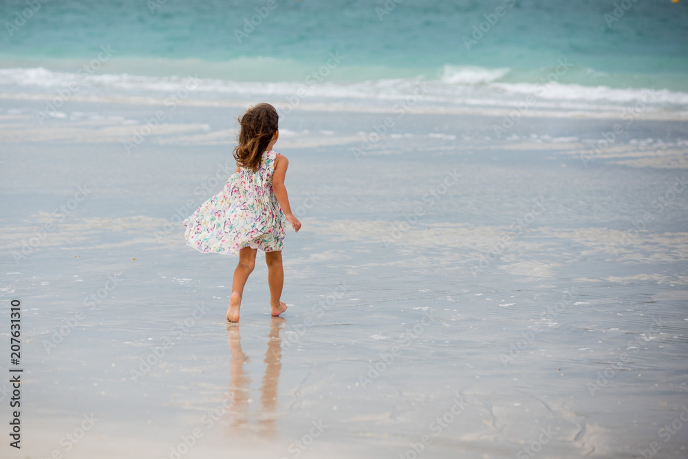Little girl runs on the beach and wear beautiful dress in cloudy day in Dubai Little girl runs on the beach and wear beautiful dress in cloudy day in Dubai