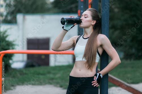 Fitness woman drinking water outdoor near sport bars