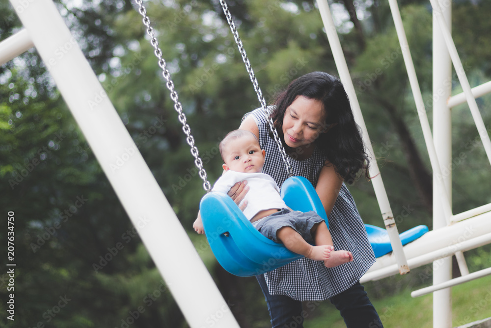 Obraz premium mother playing swing with baby on playground.