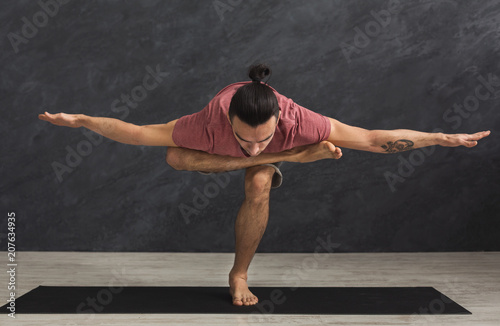 Young flexible man practicing yoga at gym photo