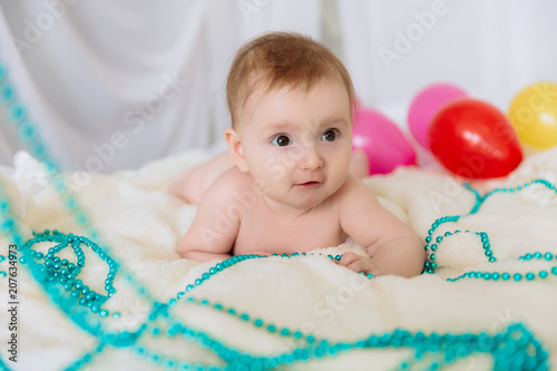 A little girl with short hair lies on the bed and plays with beads and pearls. Around her she scattered bright helium balls. photo