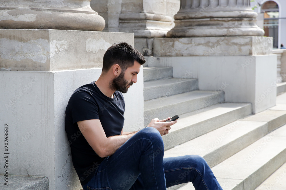 Portrait of young attractive man sitting on the stairs using mobile phone