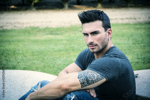 Handsome muscular man with tattoo posing in European luxury garden in Turin, Italy