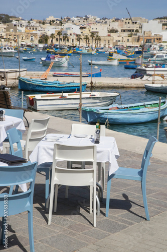 Restaurant table with colorful fishing boats in the background at Marsaxlokk Harbor, Malta