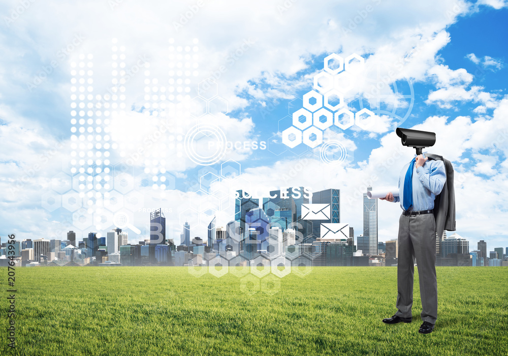 Camera headed man standing on green grass against modern cityscape