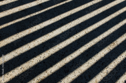 Sunlight shines through wooden fence and makes geometric stripes shadows on the ground. Shadows of wooden fence on the ground. Fence shadows texture