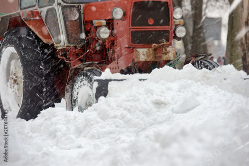 Closeup of red grader cleaning snow covered road after blizzard